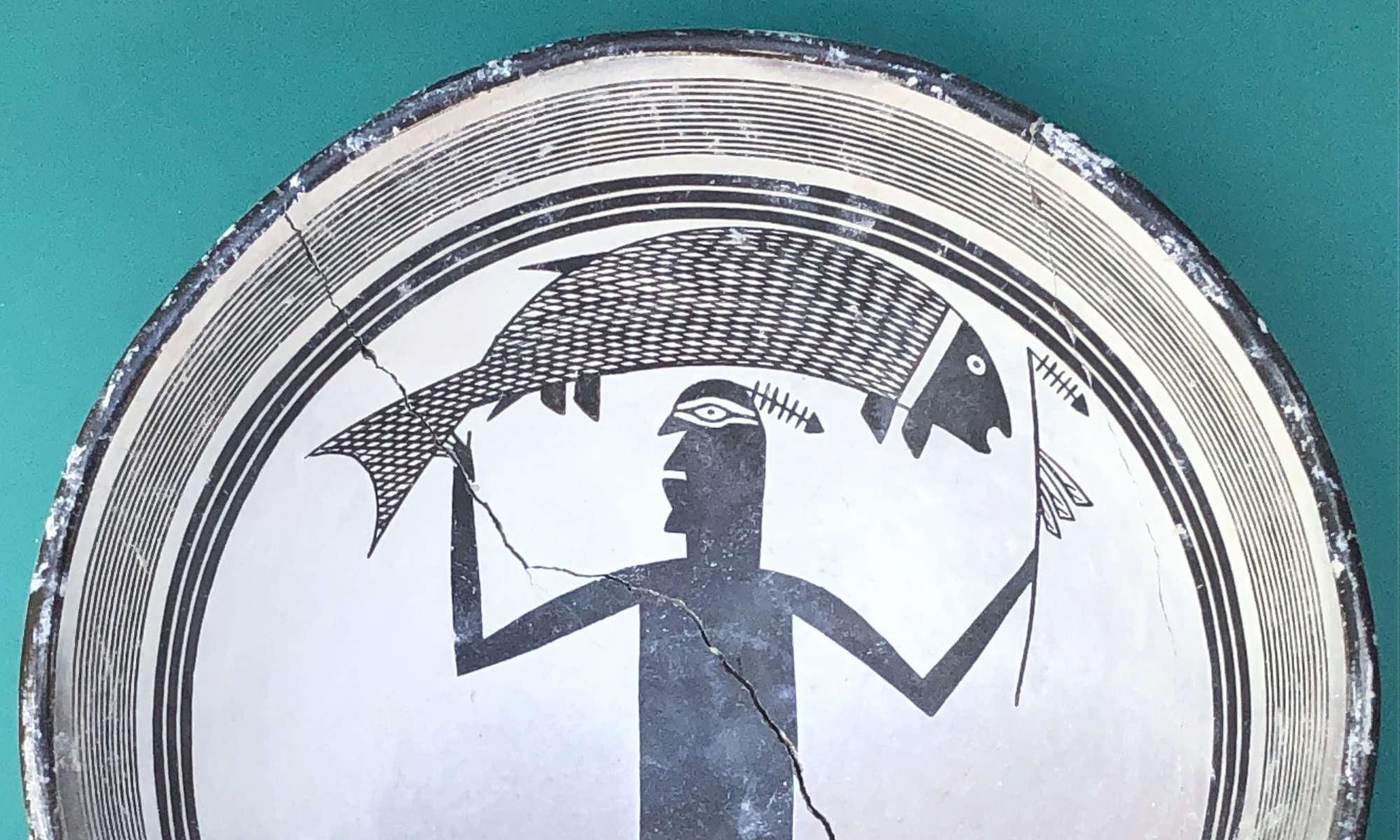 Close-up of a Native American art replica Mimbres bowl featuring a geometric figure holding a fish aloft.